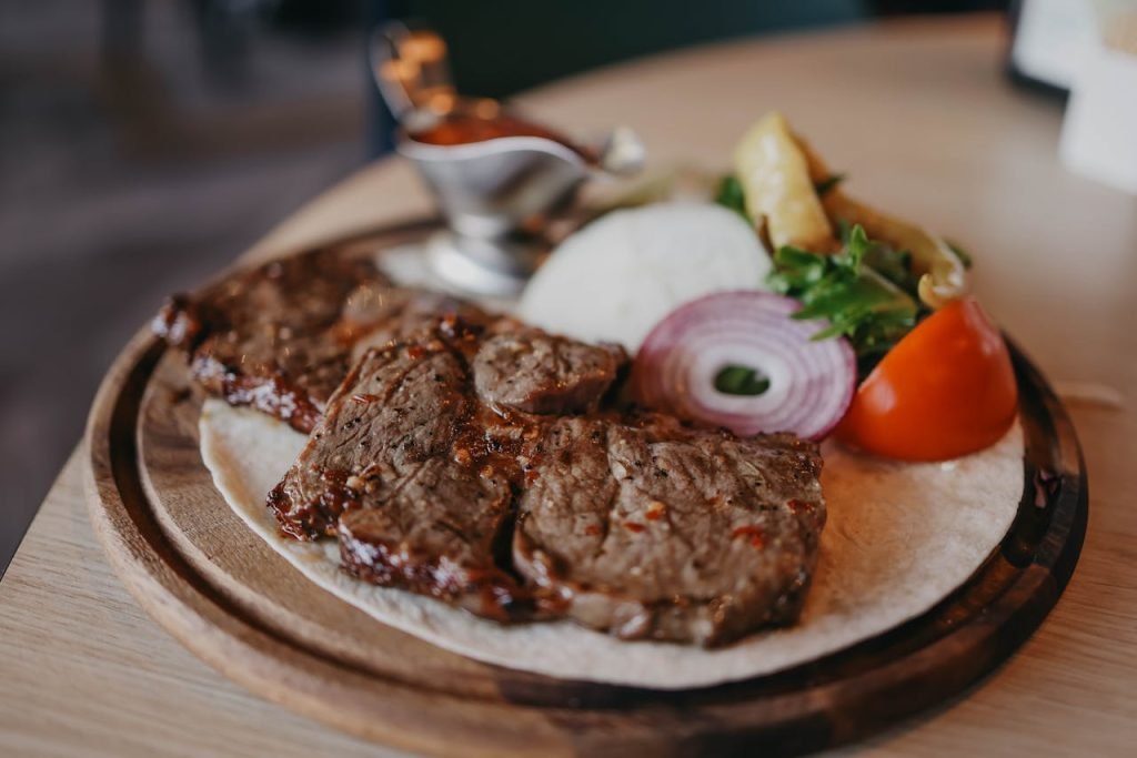 Delicious steak with fresh vegetables and tortillas on a wooden plate.