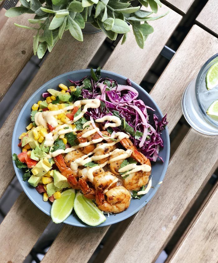 Delicious shrimp salad bowl with vibrant veggies and lime wedges on a table. Perfect for summer meals.